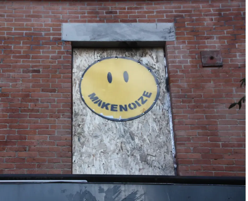 Le visage souriant de MakeNoize peint sur une fenêtre placardée. Ses œuvres sont celles d'un personnage du film.