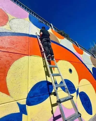 Un muraliste peint une fresque colorée depuis une échelle à Montréal-Nord.