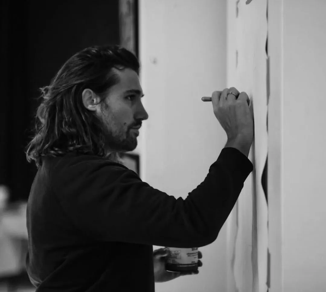 Un artiste trace un dessin au crayon sur un mur blanc.