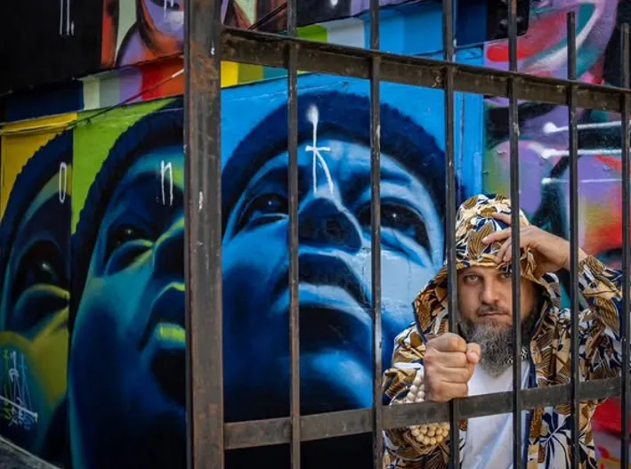 Un homme derrière une grille devant une grande murale aux teintes bleues.