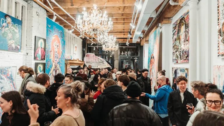 Une foule dense lors d'un vernissage dans une galerie aux murs couverts d'œuvres.